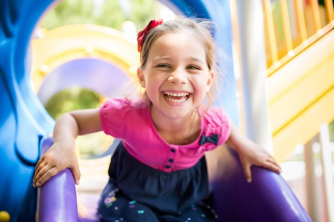 A smiling young girl on a playground slide