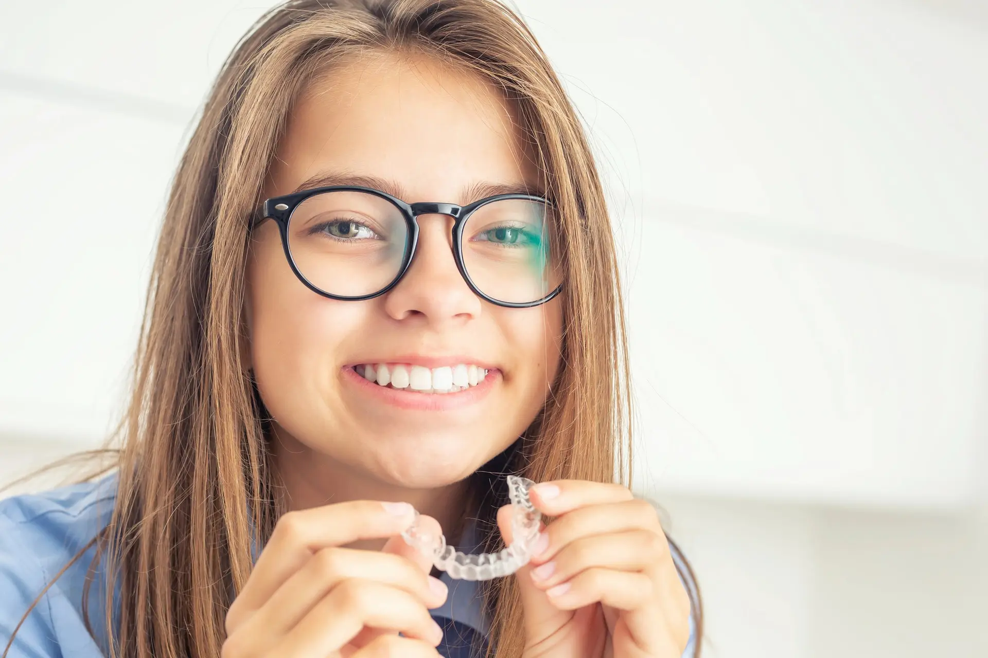 A young woman holding a clear aligner