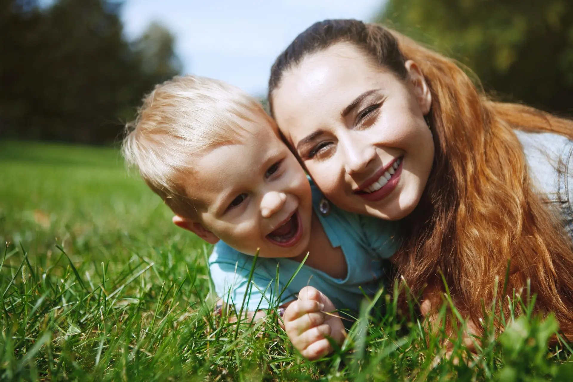 A mother and young son laughing together on the grass